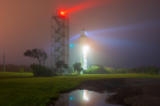 Beams of light from a lighthouse and beacon tower reflected in a pool of water on a dark foggy night