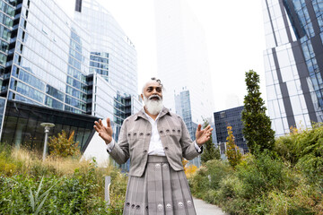 man with gray hair and beard wearing skirt suit with plants in city