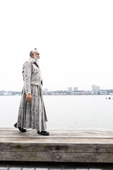 man with gray hair and beard in skirt suit walking with city view