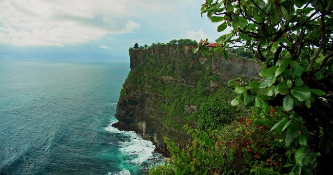 Pristine tropical green beach with Uluwatu Temple Pura Luhur Hindu on huge cliff abyss and endless ocean horizon on Bali island. Summer holiday vacation. Balinese sea water and rocky coastline.