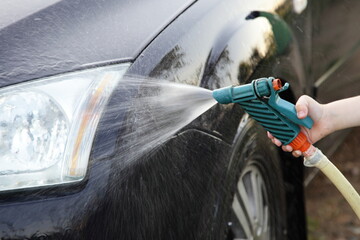 Car headlight washing outdoor with hose Garden gun sprayer in child hand at Summer