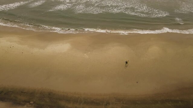 Slow-motion of surfer walking on La Pedrera beach before entering Atlantic ocean waters, Uruguay. Aerial top-down forward