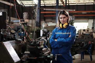 Fototapeta na wymiar Industrial worker in safety uniform with confident arms crossed, young Caucasian female engineer works with metalwork machines in manufacturing factory. Professional production mechanical occupation.