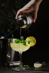 White lady alcoholic cocktail with dry gin, liquor, lemon juice and ice in glass. Bartender pours cocktail from shaker into glass. Black background
