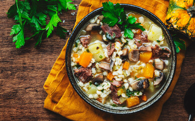 Winter comfort food. Warming soup with pumpkin, mushrooms, vegetables, beef and barley. Rustic wooden table background, top view