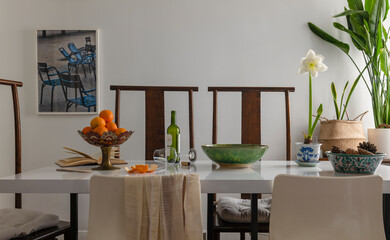 Fototapeta na wymiar Bowl of tangerines, bottle of wine, wine glass, houseplants on table in dining room