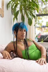indigenous non-binary artist with blue hair and braids relaxing on bed