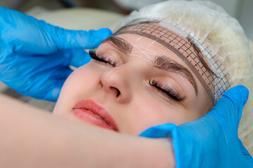 Closeup of Facial Tattoo Markup with Transparent Facial Ruler On Eyebrows of Young Caucasian Woman During a Process of Permanent make up in Salon.