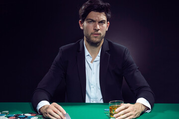 Gambling Ideas. One Concentrated Thoughful Handsome Caucasian Brunet Cards Player At Pocker Table With Chips and Cards While Playing and Drinking