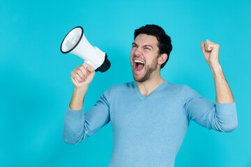 One Funny Expressive Caucasian Handsome Brunet Man Shouting Using Loudspeaker While Posing in Blue Jumper With Lifted Hand Against Blue Background