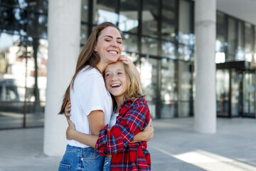 Mother hugs with daughter schoolgirl outdoors. Cheerful teen and female in good mood. Love and family concept