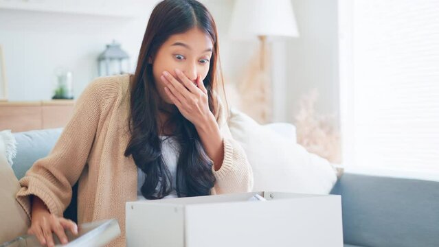 Excited young asian woman unpacking carton box and looking inside, Emotional female surprised by fast delivery service, Happy woman client satisfied with ordered purchase, Online shopping.