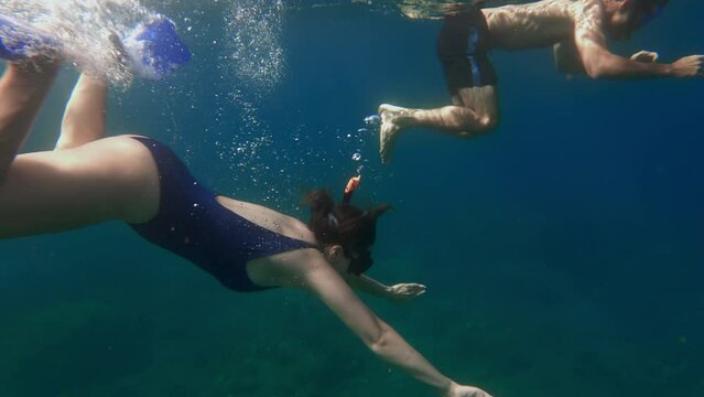 A couple snorkeling together in dark blue water of tropical sea during vacation honeymoon trip. People exploring wild nature. Woman dives to a depth in the warm ocean Film grain pixel texture.