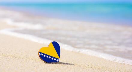 Flag of Bosnia and Herzegovina in the shape of a heart on a sandy beach.