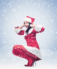 Happy young pretty girl in a red Santa costume on a light blue background of falling snow