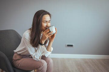 Happy smiling beautiful Asian woman enjoying first morning and smelling aroma of cup of coffee tea in her office. Enjoying free and Relax time. A good day starts with good coffee