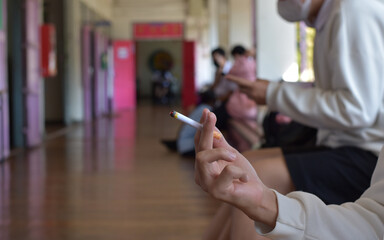 Closeup hand holding cigarette with blurred front balcony of classroom background, concept for smoking of asian young teenagers.