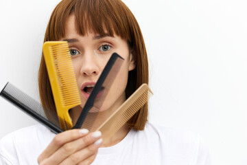 an alarmed, loudly screaming woman looks in panic at the many different combs in her hands. Horizontal studio photography, hair care topics