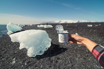 Close up tourist holding cup with ice on cold beach concept photo. First view hand photography with clear sky on background. High quality picture for wallpaper, travel blog, magazine, article