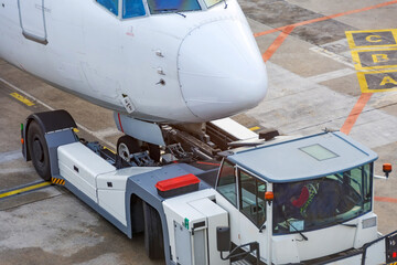 Airplane execute push back operation at airport, close up view. Tug tractor truck new type elevator...