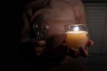 A girl in a dark room holds a candle and an electric light bulb in her hands (close-up)