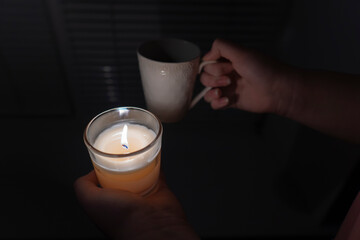 Blackout. The girl holds a candle in one hand, and a cup of tea in the other hand against the...