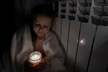 A girl holds a candle in her hands against the background of a domestic radiator. Power outage...
