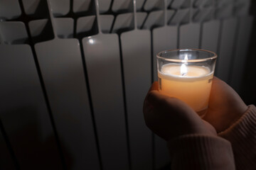 A girl holds a candle in her hands against the background of a domestic radiator. Power outage...