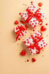St Valentine's Day concept. Top view vertical photo of present boxes with ribbon bows heart shaped candies candles and sprinkles on isolated pastel beige background