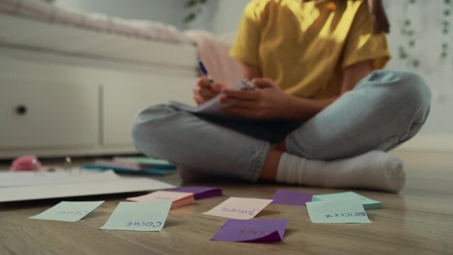 Unrecognizable caucasian teenage girl sitting on floor and making notes on flash cards. Shot with RED helium camera in 8K.   