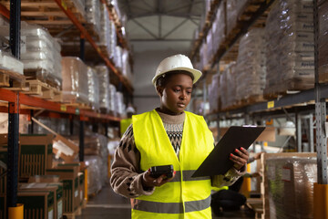 Portrait of an African-American woman working in warehouses. She is wearing safety clothes and holding a clipboard and barcode reader.