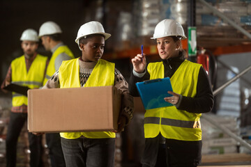 A multiracial group of people is working in a distribution warehouse, the manager is giving instructions to the workers.