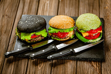 Set of three appetite color homemade burgers with marble beef with knifes on stone board.
