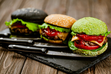  Set of three color homemade burgers with marble beef with knifes on wooden table. Selective focus 