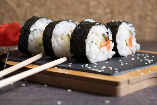 Sushi of rice, cucumber fish and cheese on a serving board with chopsticks.