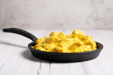 Chicken cooked in curry sauce in a black skillet on a light wooden background.