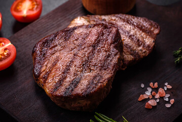 Delicious fresh juicy beef steak with spices and herbs on a dark concrete background