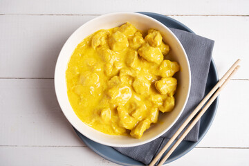 Chicken in curry sauce in a white bowl on a gray napkin with chopsticks