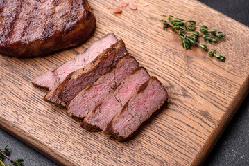 Delicious fresh juicy beef steak with spices and herbs on a dark concrete background