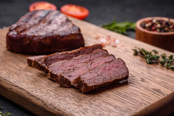 Delicious fresh juicy beef steak with spices and herbs on a dark concrete background