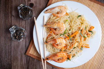 Asian funchosa salad with shrimp on a white plate with chopsticks.