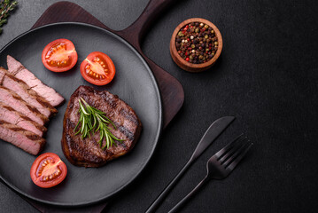 Delicious fresh juicy beef steak with spices and herbs on a dark concrete background