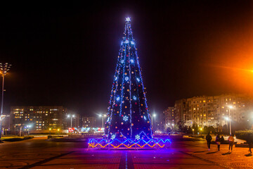 Decorated with garlands and toys, the New Year tree stands in the center of the city and glows with multi-colored illumination.