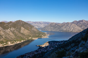Naklejka na ściany i meble Panoramic view of the bay of Kotor during sunrise in summer, Adriatic Mediterranean Sea, Montenegro, Balkan Peninsula, Europe. Fjord winding along the coastal towns. First sunbeams on Lovcen mountains