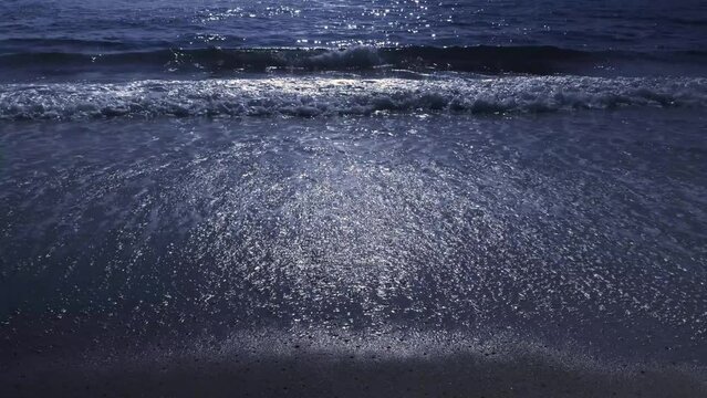 Moonlight reflecting over the sea and soft waves are sparkling waves lapping on the beach at night