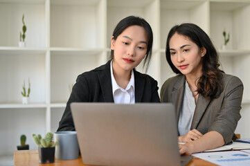 Fototapeta na wymiar Two professional and focused Asian businesswomen looking at laptop screen, working together