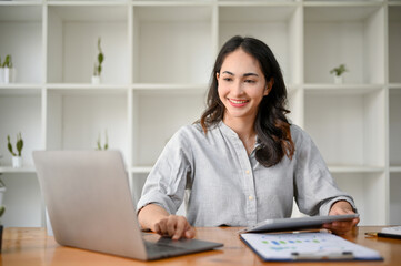 Gorgeous Asian businesswoman using laptop, reviewing business report, working at her desk