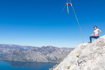 Obraz premium Woman with panoramic view from Derinski Vrh of Kotor bay in sunny summer, Adriatic Mediterranean Sea, Montenegro, Balkan Peninsula, Europe. Fjord winding along coastal towns. Lovcen, Orjen mountains