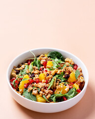 Healthy salad with spelt, oranges, pomegranate seeds. greens and nuts on light background, minimal style