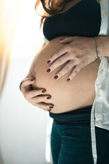 Pregnant girl caresses her baby bump. Sweet prenatal expectation. Hands touch the skin to feel the...